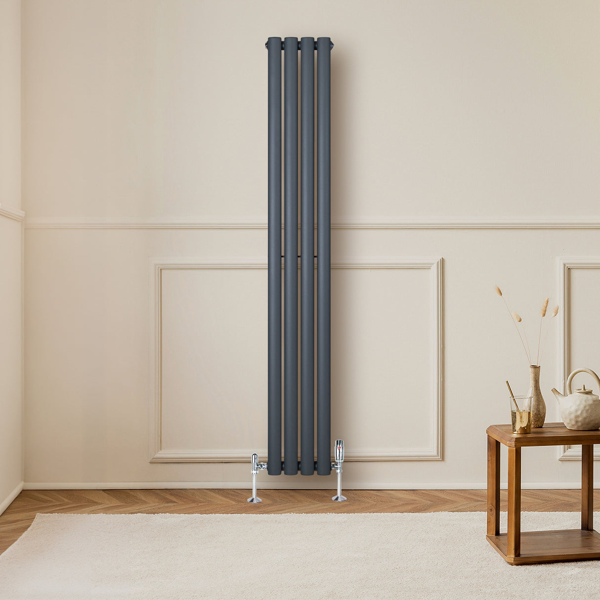 Radiador de columna ovalado en gris antracita, con cuatro tubos verticales, instalado en una pared clara junto a una mesa de madera