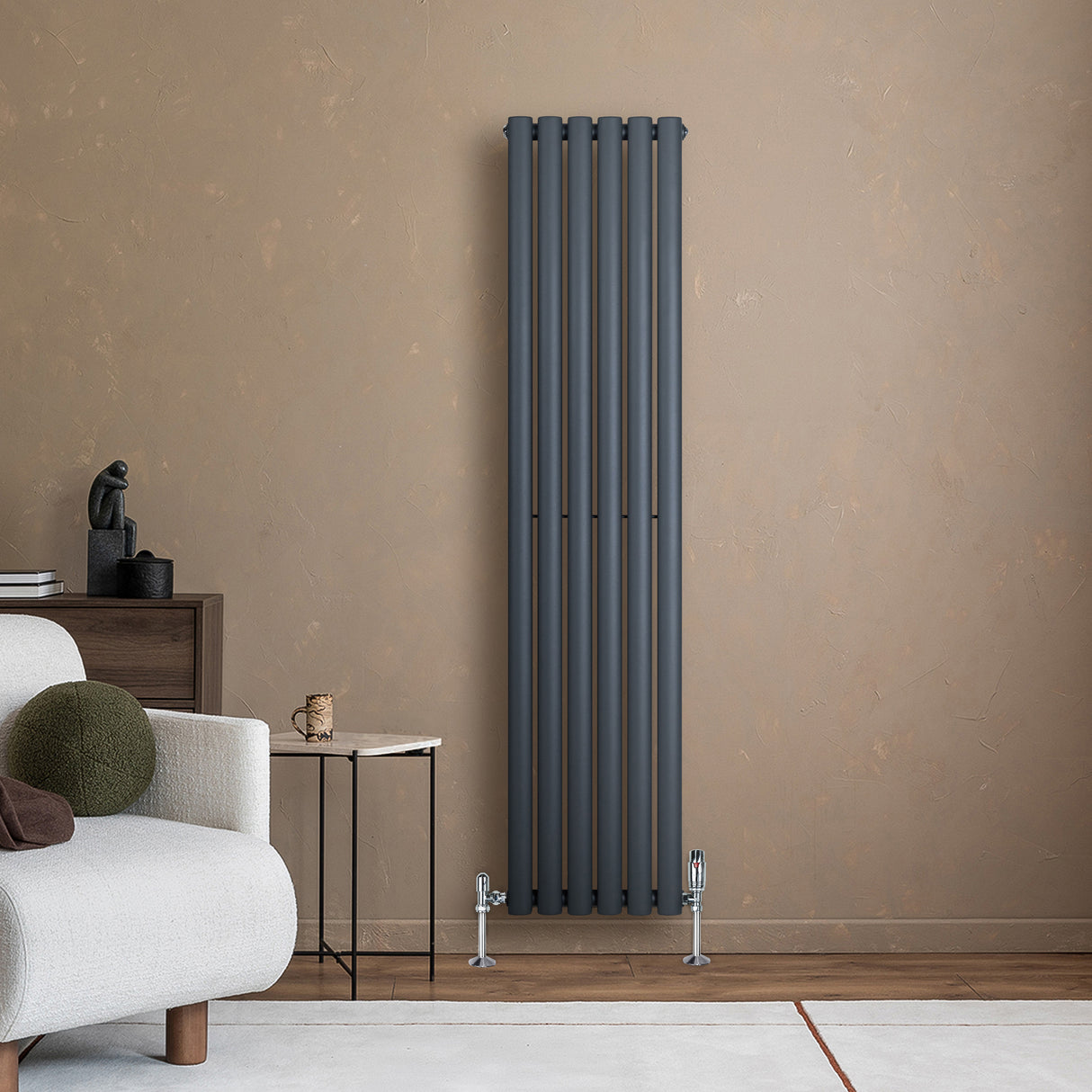 Radiador de columna ovalado en gris antracita, con diseño vertical y acabado mate, instalado junto a una pared beige y muebles modernos