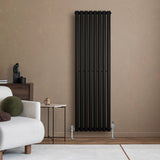 Radiador de columna ovalado negro de 1600 mm x 480 mm, con diseño moderno y acabado mate, instalado en pared beige junto a un sofá claro