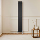 Radiador de columna ovalado negro de 1800 mm x 240 mm, con un diseño elegante y moderno, instalado en una pared clara junto a una mesa de madera