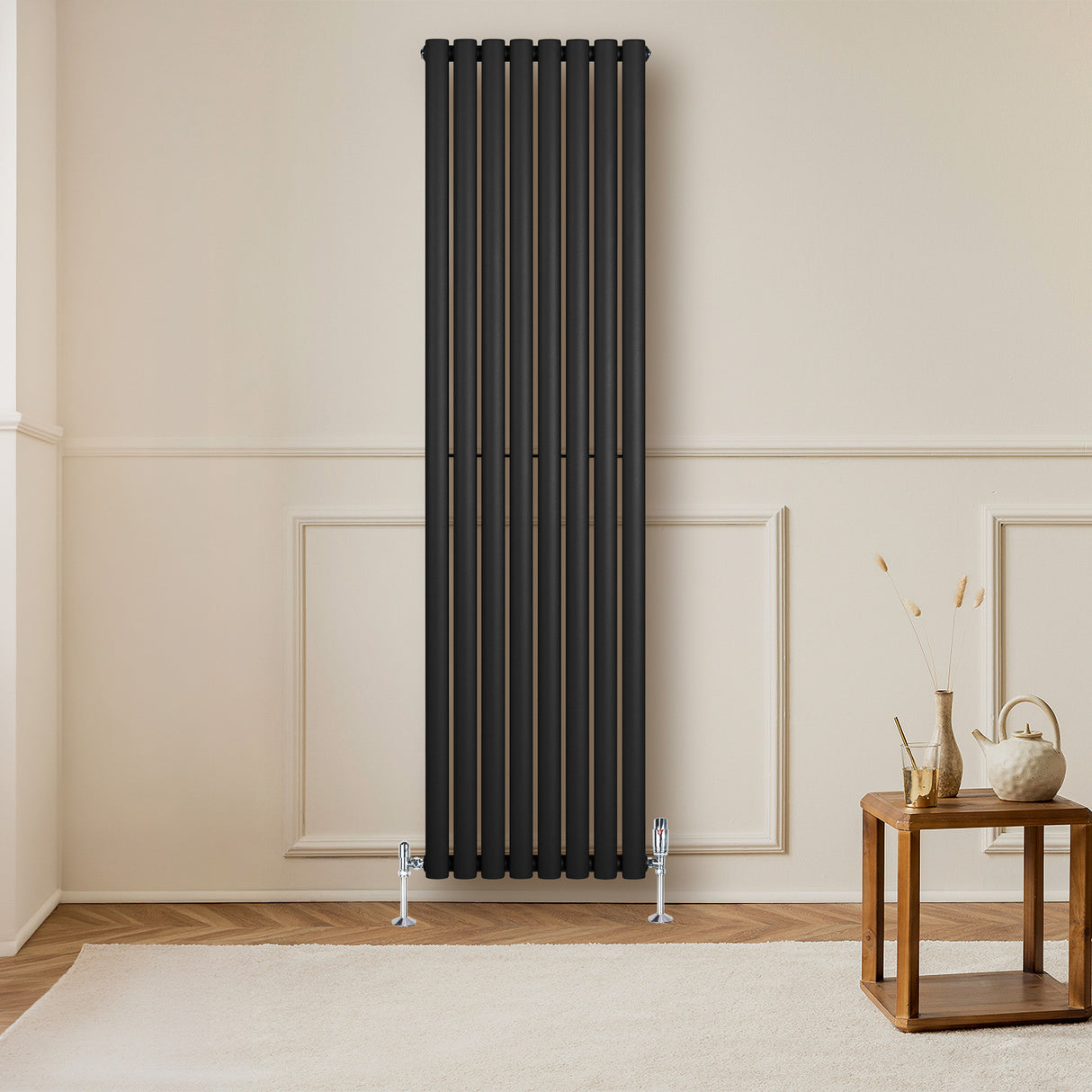 Radiador de columna ovalado negro de 1800 mm x 480 mm, con un diseño elegante y moderno, instalado en una pared clara junto a una mesa de madera