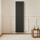 Radiador de columna ovalado negro de 1800 mm x 480 mm, con un diseño elegante y moderno, instalado en una pared clara junto a una mesa de madera