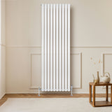 Radiador de columna ovalado blanco de 1800 mm x 600 mm, con acabado liso y elegante, instalado en una pared clara junto a una mesa de madera