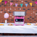 Máquina de algodón de azúcar KuKoo en color rosa, con tazón de acero inoxidable, decorada con banderines y golosinas en una mesa blanca
